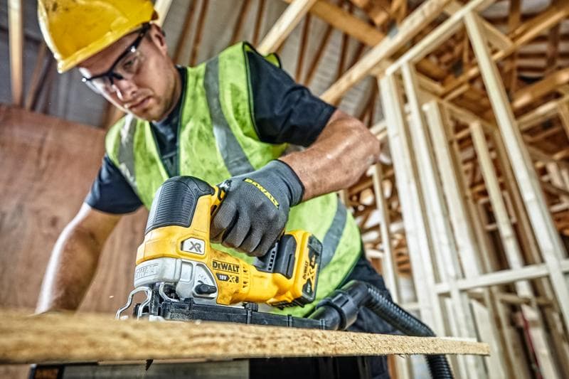 DEWALT DCS334P2 Stichsäge schneidet Holz auf Baustelle, bedient von Arbeiter mit Sicherheitsausrüstung.